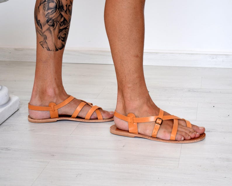 Op de afbeelding: Oranje leren sandalen met meerdere bandjes en een gespsluiting. De sandalen hebben een platte zool en zijn ontworpen voor een comfortabele pasvorm. Het schoeisel heeft een warme oranje kleur.