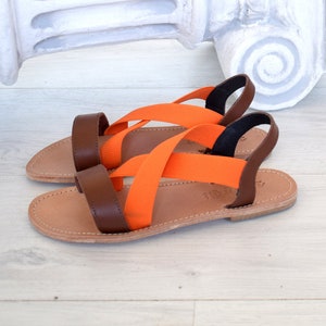 May include: A pair of brown leather sandals with orange elastic straps. The sandals have a simple design and are perfect for summer.