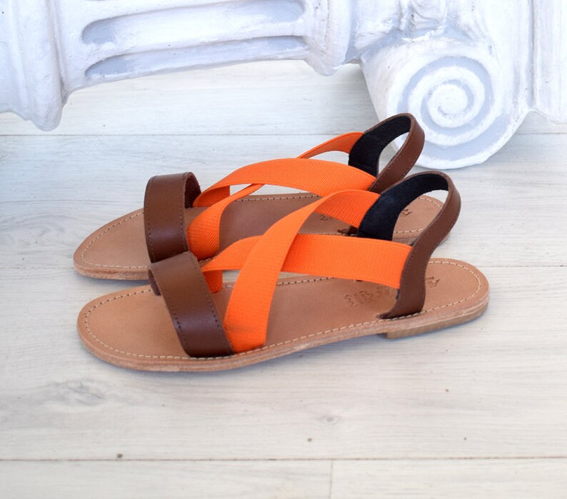 May include: A pair of brown leather sandals with orange elastic straps. The sandals have a simple design and are perfect for summer.