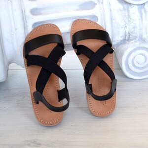 May include: Black leather sandals with criss-cross elastic straps. The sandals have a brown leather sole.