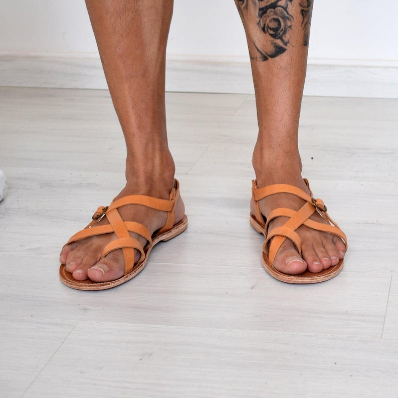 Op de afbeelding: Lichtbruine leren sandalen met gekruiste bandjes en gespsluitingen. De sandalen hebben een platte zool en zijn ontworpen voor comfort en stijl. Een klassieke keuze voor warm weer.