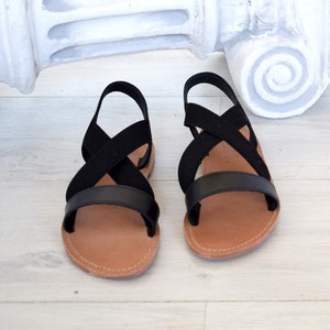 May include: Black leather sandals with criss-cross straps and a brown sole.