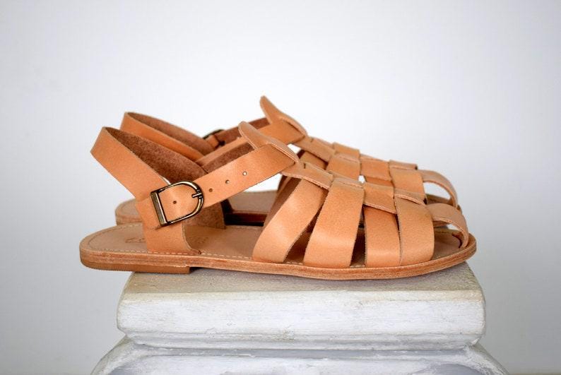 May include: A pair of light brown leather sandals with a woven design and adjustable ankle straps. The sandals have a buckle closure and are displayed on a white surface.