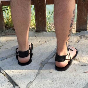 May include: A pair of black leather sandals with adjustable straps. The sandals are worn on a person's feet.