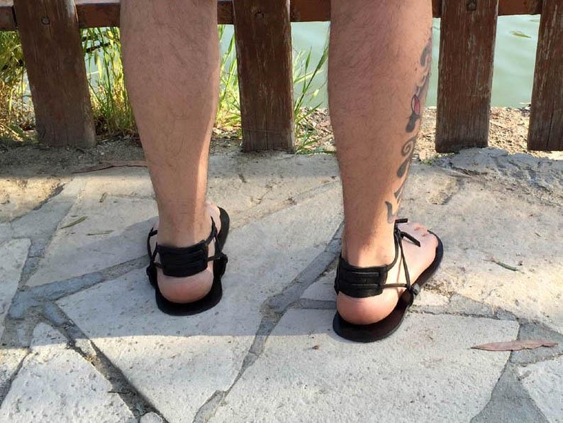 May include: A pair of black leather sandals with adjustable straps. The sandals are worn on a person's feet.