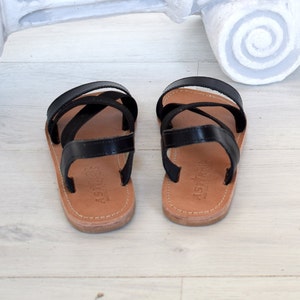 May include: A pair of black leather sandals with criss-cross straps. The sandals have a brown leather sole and are made by the brand "Astra"