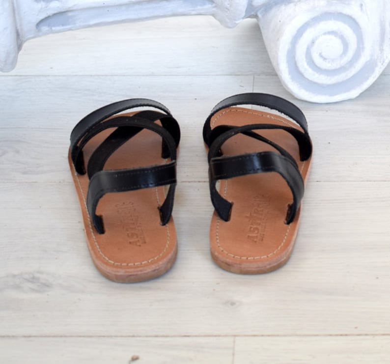 May include: A pair of black leather sandals with criss-cross straps. The sandals have a brown leather sole and are made by the brand "Astra"