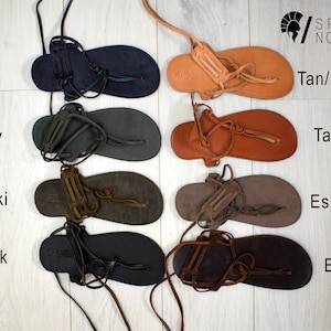 Puede incluir: Variedad de sandalias de cuero en varios colores, incluyendo azul, gris, caqui, negro, tan/natural, tampa, espresso y marr&oacute;n. Cada sandalia presenta un dise&ntilde;o de tipo chancla con correas y suela plana. Las sandalias se exhiben sobre una superficie de madera clara.