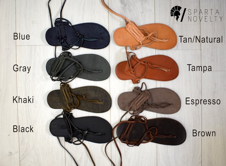 Puede incluir: Variedad de sandalias de cuero en varios colores, incluyendo azul, gris, caqui, negro, tan/natural, tampa, espresso y marr&oacute;n. Cada sandalia presenta un dise&ntilde;o de tipo chancla con correas y suela plana. Las sandalias se exhiben sobre una superficie de madera clara.