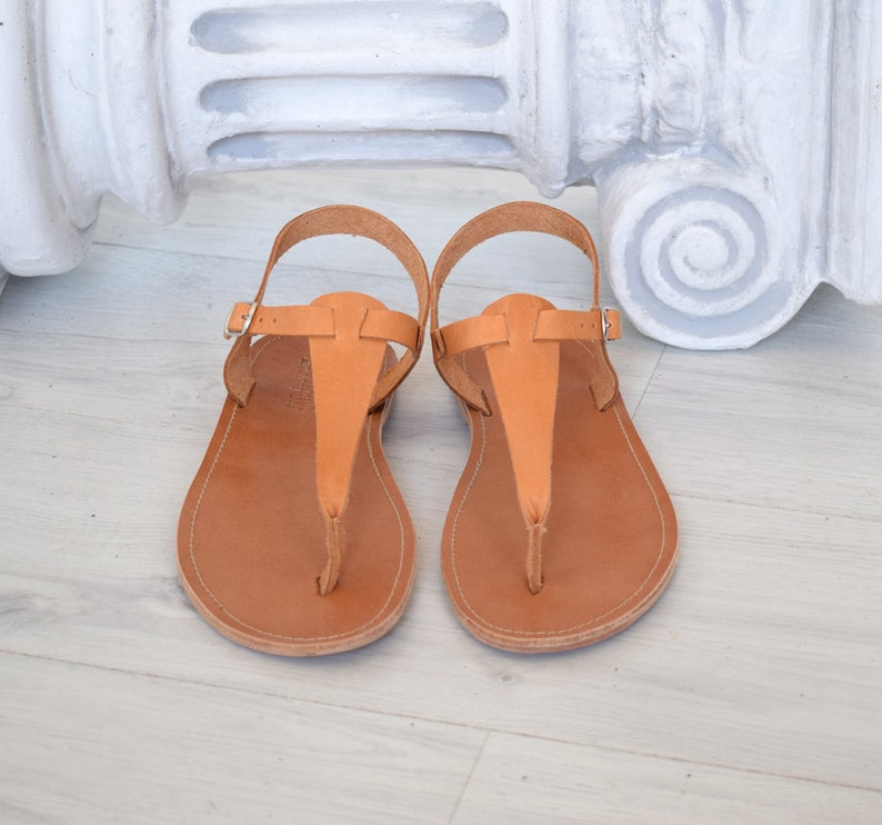 May include: A pair of brown leather sandals with a t-strap design. The sandals have a simple, minimalist style and are perfect for warm weather.