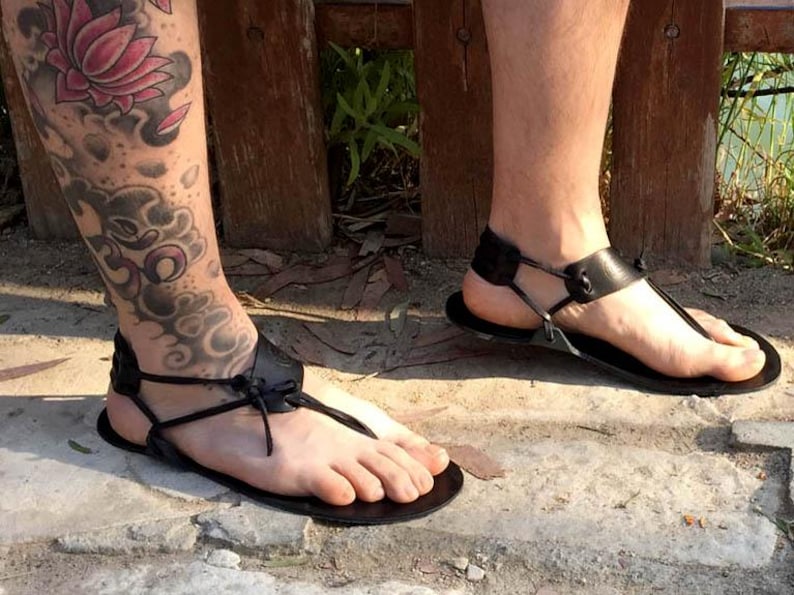 May include: A pair of black leather sandals with adjustable straps and buckles. The sandals are worn on a person's feet, and the straps are tied around the ankles.