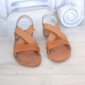 May include: A pair of brown leather sandals with criss-cross straps. The sandals have a simple design and are perfect for summer.