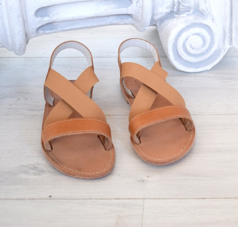 May include: A pair of brown leather sandals with criss-cross straps. The sandals have a simple design and are perfect for summer.