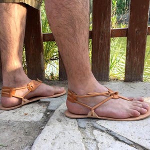 May include: A pair of brown leather sandals with a simple design and adjustable straps. The sandals are worn on a person's feet, with the toes visible.