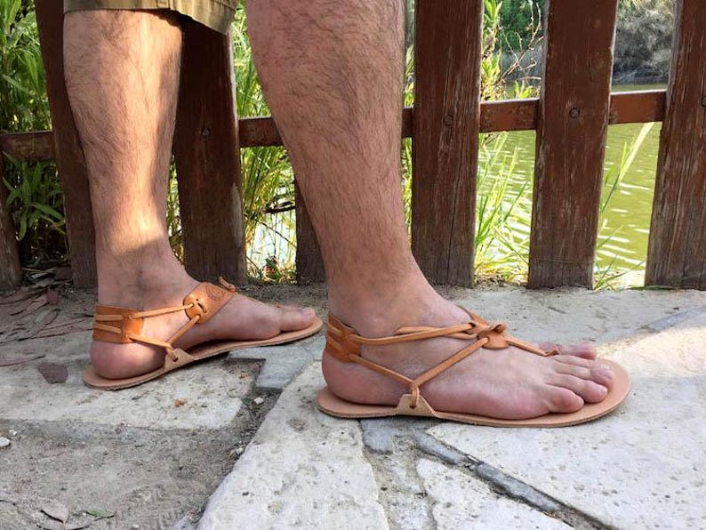 May include: A pair of brown leather sandals with a simple design and adjustable straps. The sandals are worn on a person's feet, with the toes visible.
