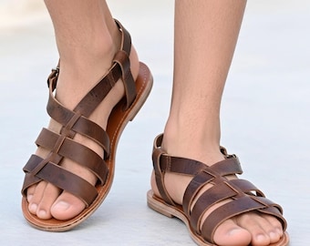May include: Brown leather sandals with multiple straps and a buckle closure. The sandals have a flat sole and are designed for comfort and style. The image shows the sandals on a person's feet.