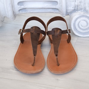 May include: A pair of brown leather sandals with a t-strap design. The sandals have a simple, minimalist style and are perfect for warm weather.