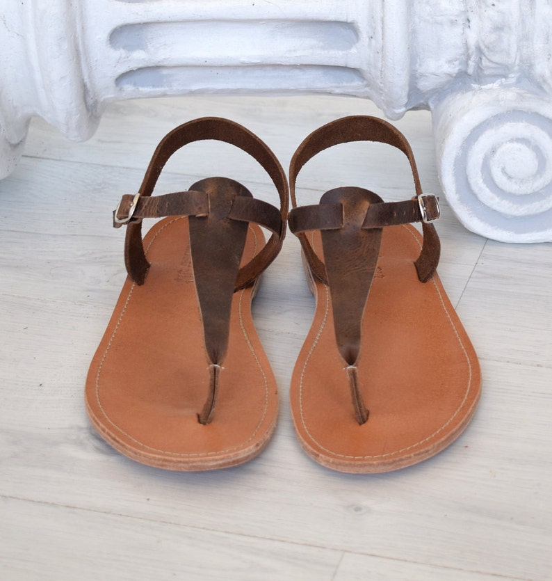 May include: A pair of brown leather sandals with a t-strap design. The sandals have a simple, minimalist style and are perfect for warm weather.