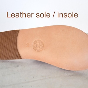 Puede incluir: Una suela y plantilla de cuero color canela para sandalia, con una secci&oacute;n de tal&oacute;n texturizada en marr&oacute;n y un logotipo circular en relieve con el n&uacute;mero 38 en el centro. El texto "Leather sole / insole" est&aacute; impreso en marr&oacute;n arriba.
