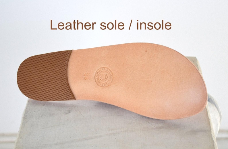 Puede incluir: Una suela y plantilla de cuero color canela para sandalia, con una secci&oacute;n de tal&oacute;n texturizada en marr&oacute;n y un logotipo circular en relieve con el n&uacute;mero 38 en el centro. El texto "Leather sole / insole" est&aacute; impreso en marr&oacute;n arriba.