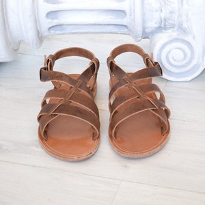 May include: A pair of brown leather sandals with multiple straps and a buckle closure. The sandals have a light brown sole and are designed for comfort and style. The sandals are approximately 8 inches long.