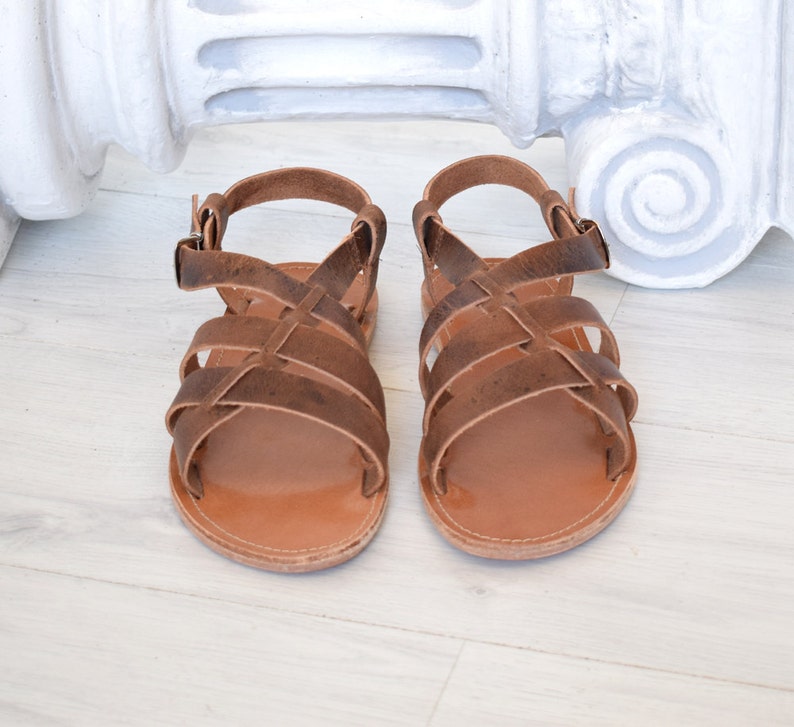 May include: A pair of brown leather sandals with multiple straps and a buckle closure. The sandals have a light brown sole and are designed for comfort and style. The sandals are approximately 8 inches long.