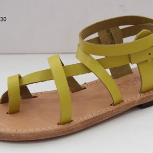 Op de afbeelding: Gele leren sandalen met meerdere banden en een gespsluiting. De sandalen hebben een platte zool en zijn gemaakt van leer.