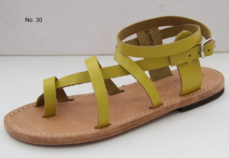Op de afbeelding: Gele leren sandalen met meerdere banden en een gespsluiting. De sandalen hebben een platte zool en zijn gemaakt van leer.