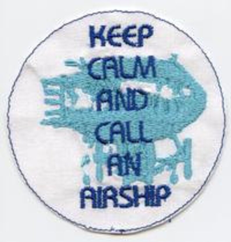 May include: White round embroidered patch with blue text that reads "Keep Calm and Call an Airship".