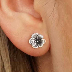 May include: A pair of silver flower stud earrings. The earrings are small and delicate, with a five-petal flower design.