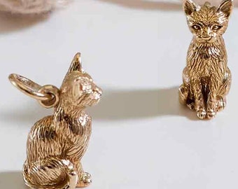 May include: Two gold-colored cat figurines. One cat is sitting upright, while the other is sitting with its tail curled around its legs. Both cats have detailed fur and realistic features.
