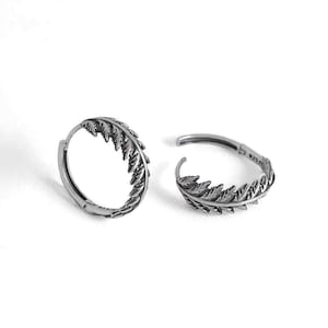 May include: A pair of silver hoop earrings with a leaf design. The earrings are made of metal and have a polished finish.