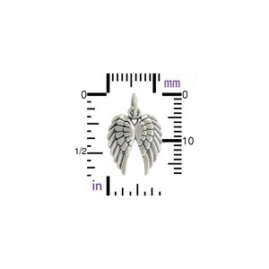 May include: A silver-colored wing charm, approximately 0.5 inches wide, with detailed feather textures. The charm has a small loop at the top for attachment. A ruler with inch and millimeter measurements is in the background.