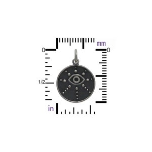 May include: A silver charm with a black enamel eye design. The eye is surrounded by a circle of small dots. The charm is 2 cm in diameter.