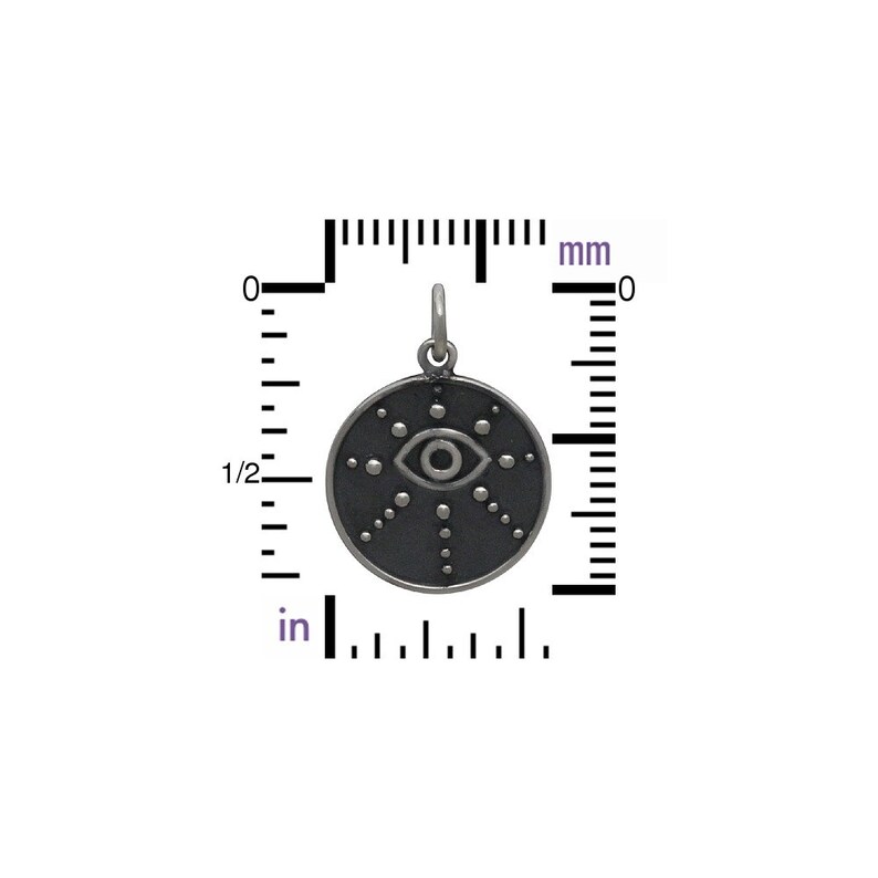 May include: A silver charm with a black enamel eye design. The eye is surrounded by a circle of small dots. The charm is 2 cm in diameter.