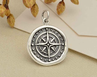 May include: A silver charm featuring a compass design. The compass has a four-pointed star at its centre and is encircled by a ring of dots.