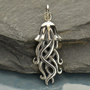 May include: A silver charm in the shape of a jellyfish with a detailed, intricate design. The charm has a bell-shaped top and long, flowing tentacles.