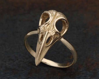 May include: A gold ring with a detailed bird skull design. The skull is three-dimensional and has a hollowed-out appearance.