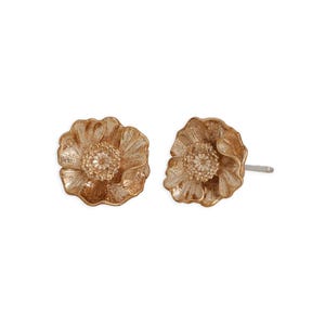 May include: A pair of gold-colored flower stud earrings. Each earring features a detailed, textured flower design with a central, textured, lighter-colored center. The earrings are set against a white background.