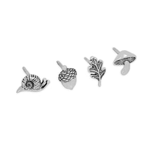 May include: A set of four silver-toned stud earrings. The earrings feature a snail, an acorn, an oak leaf, and a mushroom. The earrings are small and detailed, perfect for nature lovers.