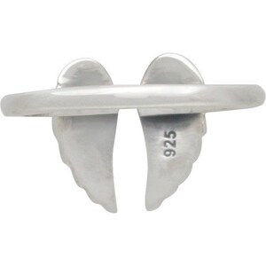 May include: A silver ring featuring a pair of stylized angel wings. The ring's band is smooth and connects the wings, which are detailed with feather-like textures. The number "925" is stamped on one of the wings, indicating the metal's purity.