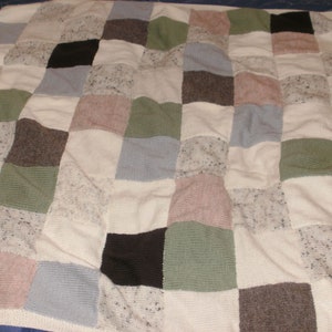 May include: A patchwork quilt featuring a variety of neutral-toned squares. The squares include shades of white, gray, brown, green, and pink. The quilt is made of different textured fabrics, creating a cozy and inviting appearance.