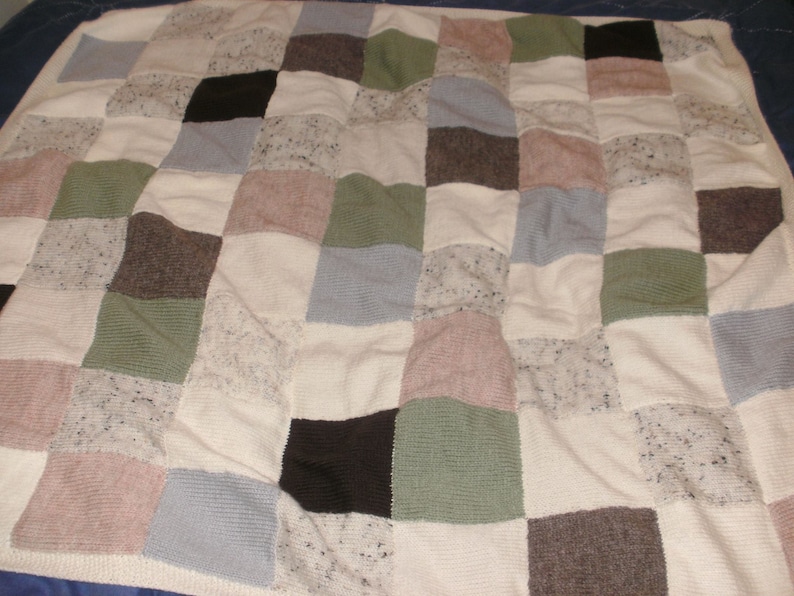 May include: A patchwork quilt featuring a variety of neutral-toned squares. The squares include shades of white, gray, brown, green, and pink. The quilt is made of different textured fabrics, creating a cozy and inviting appearance.
