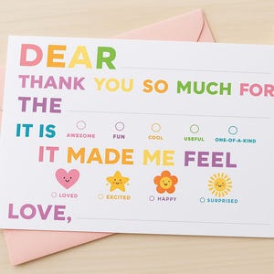 May include: A thank you card with colorful text and a pink envelope. The card reads "DEAR THANK YOU SO MUCH FOR THE IT IS IT MADE ME FEEL LOVE," with options to select how the recipient felt. A cat-shaped pen rests on the right.