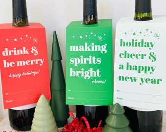 May include: Three Christmas-themed wine bottle gift tags with festive sayings. The tags are red, green, and white with a snowflake and star design. The text on the tags reads "drink & be merry", "making spirits bright", and "holiday cheer & a happy new year".