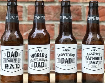 May include: Four brown glass beer bottles with white labels and black text. The labels have different messages for Father's Day, including "Dad You're Rad", "World's Greatest Dad", "I Love You Dad", and "Happy Father's Day 2018".