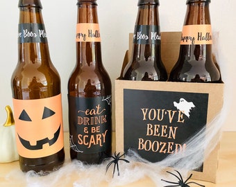 May include: Four brown glass beer bottles with Halloween-themed labels. The labels are black with orange and white text and graphics. The labels say "Eat Drink & Be Scary", "You've Been Boozed", and "Happy Halloween".