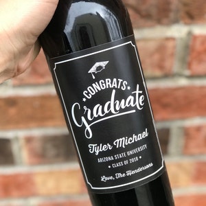 May include: A black wine bottle with a white label that says "Congrats Graduate" with a graduation cap icon. The label also says "Tyler Michael, Arizona State University, * Class of 2018 * Love, The Hendersons".