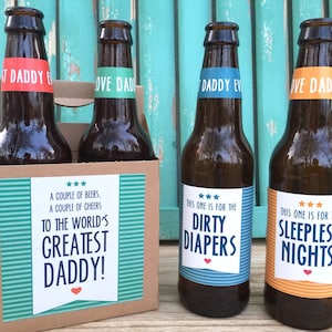 May include: Four brown glass beer bottles with colorful labels. The labels have text that reads "To the World's Greatest Daddy!" and "This one is for the Dirty Diapers" and "This one is for the Sleepless Nights".