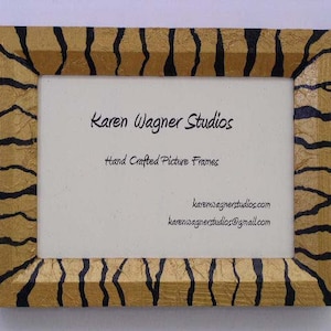 May include: A gold picture frame with black tiger stripes. The frame has a white mat and the text "Karen Wagner Studios" and "Hand Crafted Picture Frames" is printed in black. The text "karenwagnerstudios.com" and "karenwagnerstudios@gmail.com" is printed in black at the bottom of the mat.